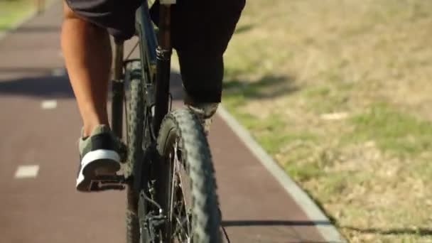 Zadní pohled na muže s umělou nohou cyklistika podél greenway — Stock video
