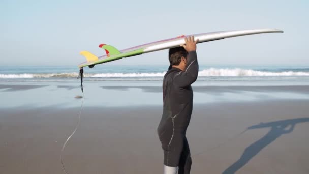 Vista lateral del hombre con discapacidad caminando en la playa con tabla de surf — Vídeos de Stock