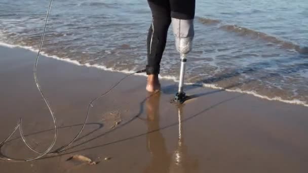 Bakåt bild av man med bionic ben in i havet med surfbräda — Stockvideo