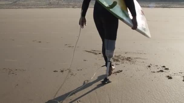 Surfista con disabilità che tiene la tavola da surf sotto braccio sull'oceano — Video Stock