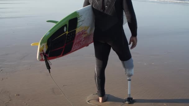 Vista posteriore del surfista maschio con bionico in piedi sulla riva dell'oceano — Video Stock