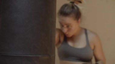 Orta boy boks eldivenli bir kadın kum torbasına vuruyor.