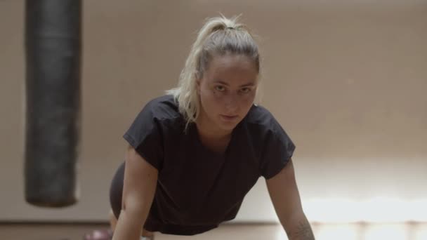 Mujer confiada mirando a la cámara mientras hace flexiones en el gimnasio — Vídeos de Stock