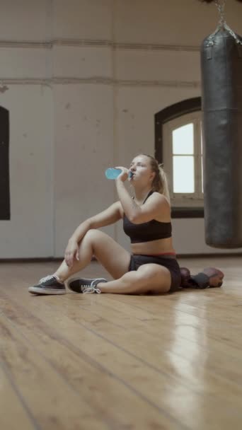 Pionowe ujęcie wyczerpanej kobiety pijącej izotonik na siłowni — Wideo stockowe