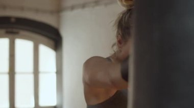 Odaklanmış kadının spor salonunda kum torbasına vurması ön planda.