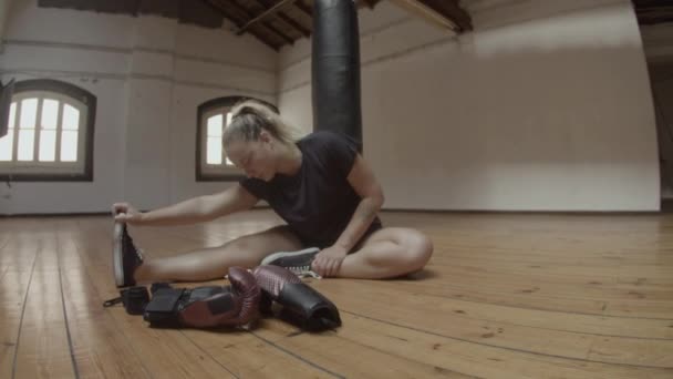 Long shot de kickboxer féminin étirant les jambes sur le sol dans la salle de gym — Video