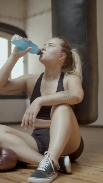 Pionowe ujęcie ciężko oddychającej kobiety pijącej izotonik na siłowni — Wideo stockowe
