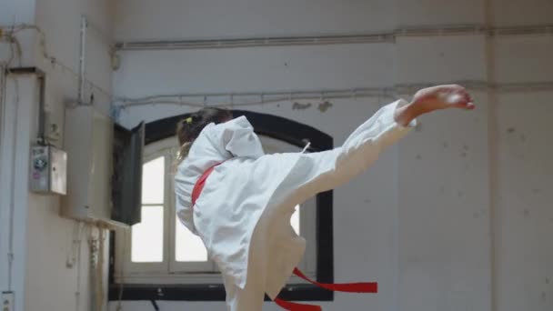 Zijaanzicht van gerichte karateka doen schoppen met twist in de sportschool — Stockvideo