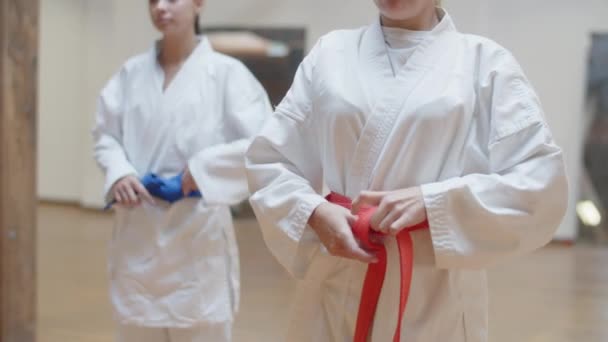Вид сфокусированных девушек, завязывающих красные и синие пояса на кимоно — стоковое видео