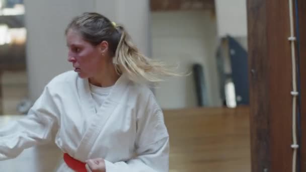Tracking shot of serious girl in kimono practicing kicks in gym — Stock Video
