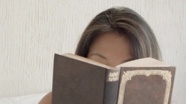 Güzel bir kadının kitap okuması ve kameraya bakması.