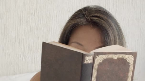 Vista frontal de la mujer bonita leyendo libro y mirando a la cámara — Vídeos de Stock