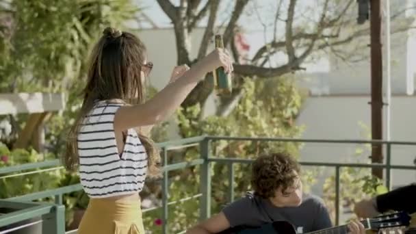 Boldog lány táncol a tetőtéri partin, míg a férfiak gitároznak — Stock videók