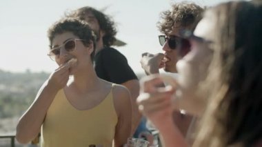 Neşeli adam ve kadınlar çatıdaki partide ev yapımı pizza tadıyorlar. 