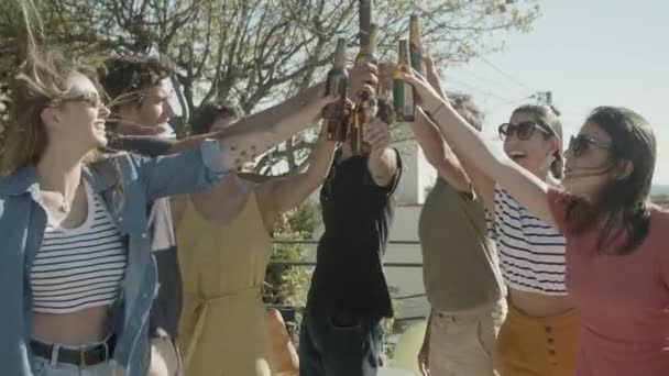 Улыбающиеся друзья, поднимающие бутылки пива во время вечеринки на крыше — стоковое видео