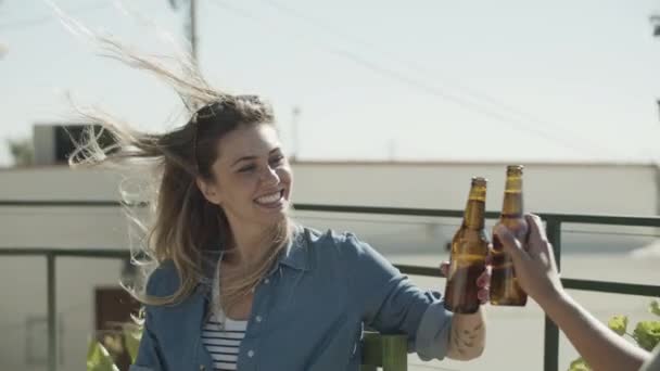 Mujeres felices sentadas en la azotea y tintineando botellas de cerveza — Vídeos de Stock