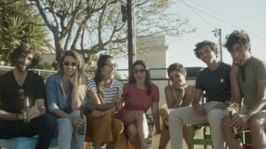 Mutlu arkadaşlar terasta oturur ve kameraya bakarlar.