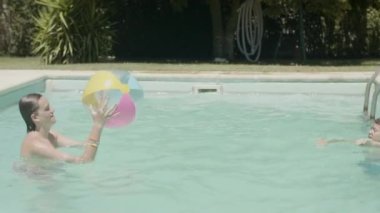 Mutlu beyaz gençler yüzme havuzunda top oynuyorlar.