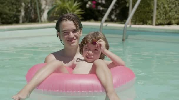 Boy with little brother on inflatable tube in swimming pool — Stockvideo