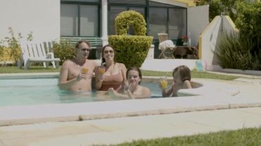 Kafkas ailesi yüzme havuzunda kokteyl bardaklarını tokuşturuyor. 