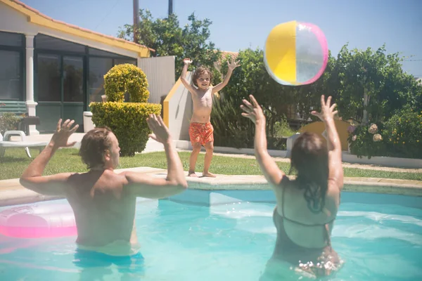 Genitori felici e figlio che giocano a palla in piscina — Foto Stock