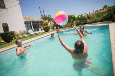 Neşeli aile yüzme havuzunda top oynuyor