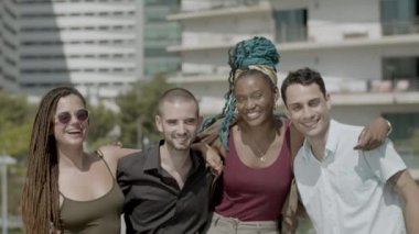 Gülümseyen iş arkadaşlarının kucaklaşması ve kameraya bakması ön planda.