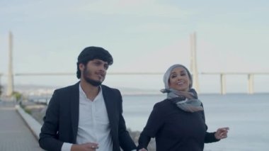 Okyanusun yanında koşup el ele tutuşan neşeli Arap âşıklar.