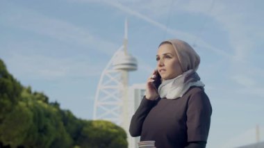 Tesettürlü güzel bir kadın kahve içiyor ve telefonda konuşuyor.