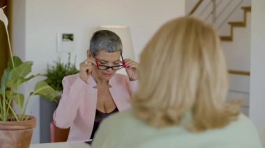 Ciddi bir emlakçı evde masada oturuyor ve gözlük takıyor.