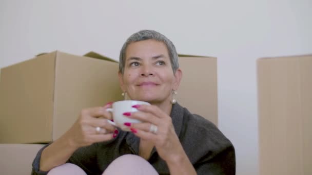 Cheerful woman sitting on floor and holding cup of tea in hands — Stock Video