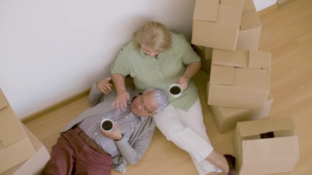 Κουρασμένο ζευγάρι ηλικιωμένων ξαπλωμένο στο πάτωμα και πίνοντας τσάι μετά τη μετακίνηση — Αρχείο Βίντεο