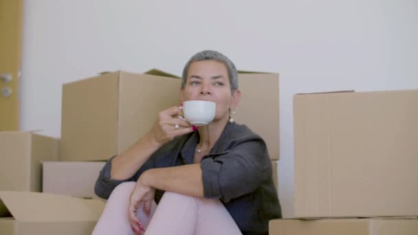 Mujer sentada en el suelo, bebiendo té después de mudarse a casa nueva — Vídeo de stock