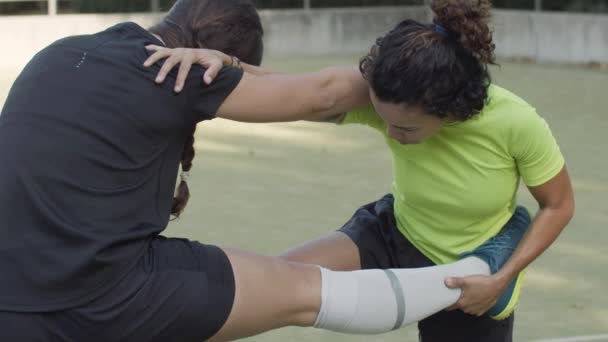 Женщины держат друг друга за плечо и вытягивают ноги на открытом воздухе — стоковое видео