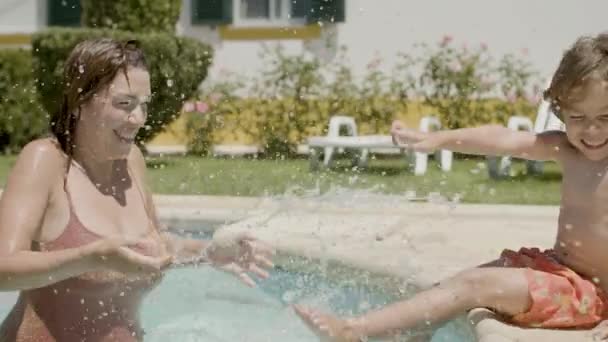 Ragazzo seduto sul bordo della piscina e spruzzi d'acqua con i genitori — Video Stock