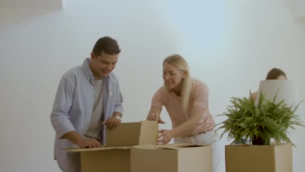 Взволнованные жена и муж вытаскивают вещи из коробок после переезда — стоковое видео
