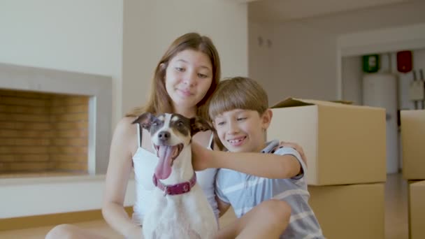Happy kids sitting on floor and stroking dog at home — Stock Video