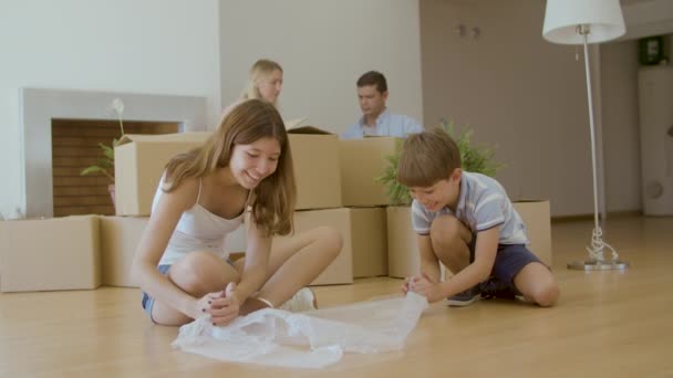 Cute kids sitting on floor and bursting bubble wrap after moving — Stock Video