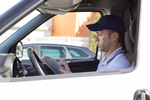 Serious deliveryman signing documents in car — Stock Photo, Image