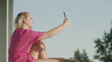 Gülümseyen kız telefonda kaykay üstüne selfie çekiyor.