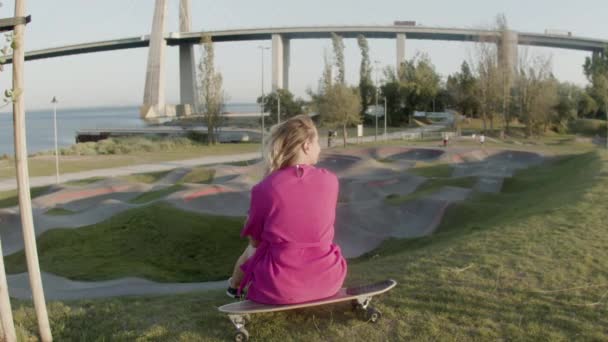 Piękna dziewczyna w sukience siedzi na longboard w skate parku — Wideo stockowe