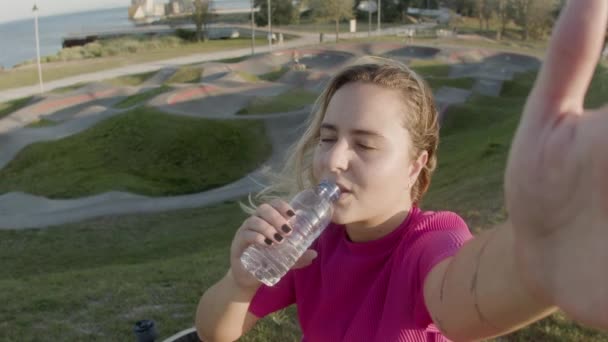 Chica bebiendo agua en el parque de skate y grabación de vídeo en el teléfono — Vídeo de stock