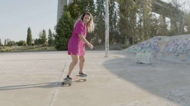 Menina focada com fones de ouvido montando longboard no skatepark — Vídeo de Stock