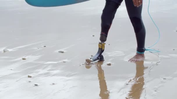 Felismerhetetlen szörfös műlábbal a tengerparton sétálva — Stock videók