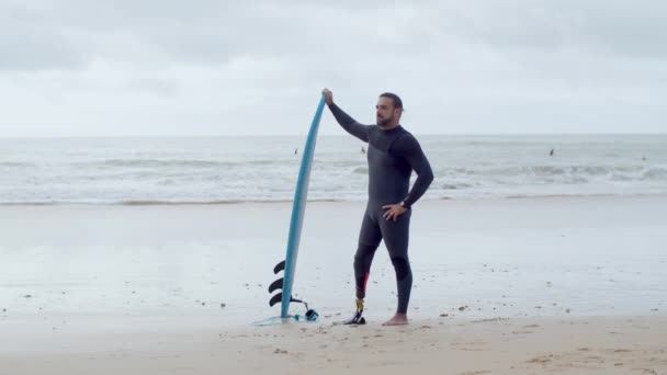 Surfista alegre con pierna artificial de pie en la playa de arena — Vídeos de Stock
