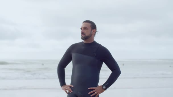 Guapo surfista en forma de pie en la orilla del mar con las manos en los lados — Vídeos de Stock