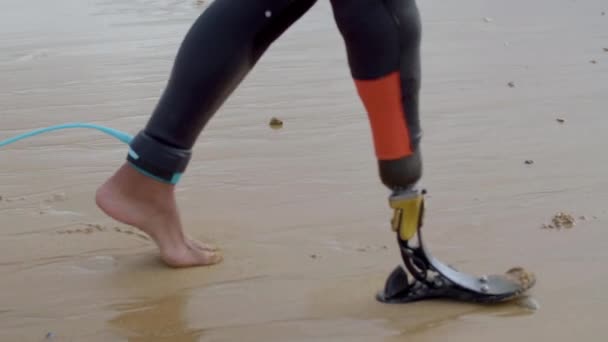 Adatto surfista con gamba bionica che cammina lungo la riva del mare — Video Stock