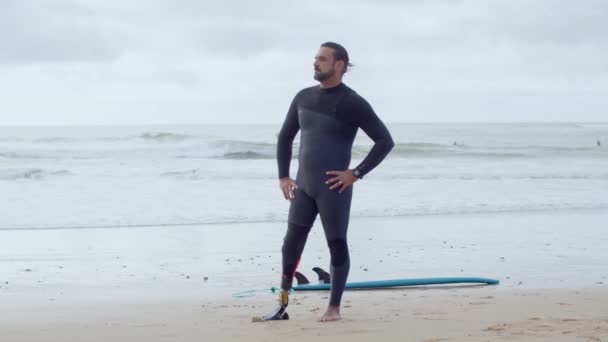 Ajuste surfista en traje de neopreno con pierna biónica de pie en la playa del océano — Vídeos de Stock