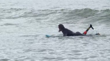 Yapay bacaklı bir adam okyanusta sörf tahtasında kürek çekiyor.