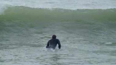 Engelli bir adam sörf tahtasında yatarken dalgalar onu koruyor.